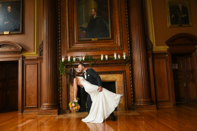 The groom dips the bride back in front of the fireplace